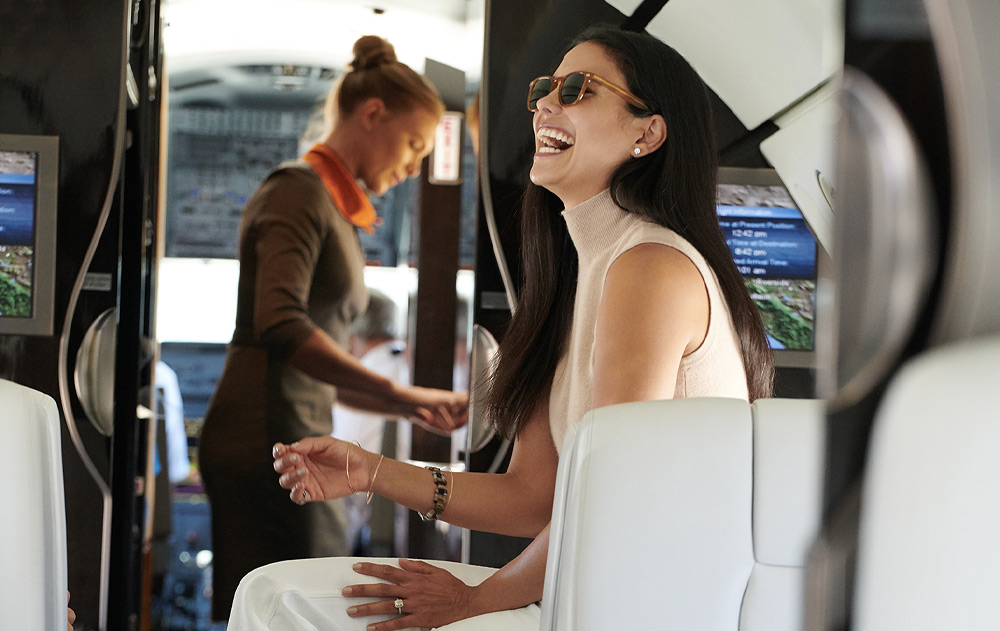 woman laughing inside of private jet, cabin attendant in background